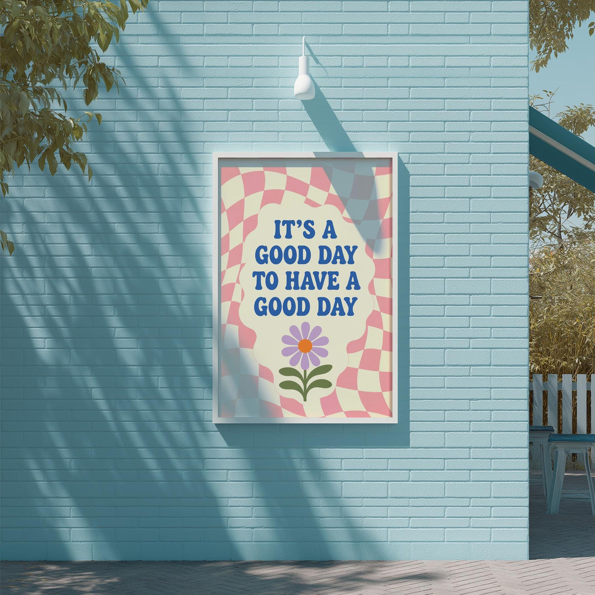A framed poster with the text "IT'S A GOOD DAY TO HAVE A GOOD DAY" and a flower design is displayed on a blue brick wall.