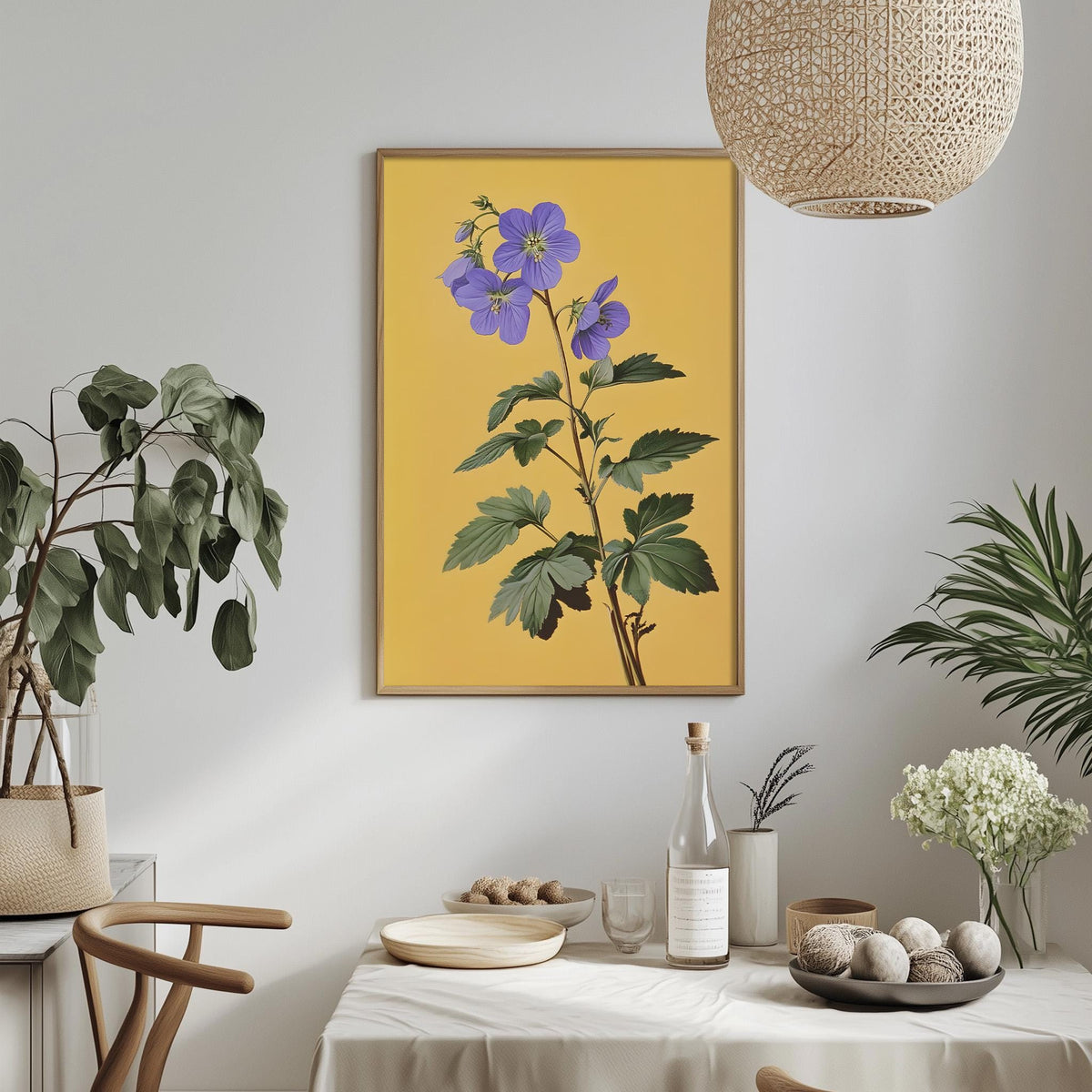 a dining table with a white tablecloth, a bowl of fruit, a bottle, and a vase with flowers. Above the table, there is a framed picture of a plant with purple flowers. The table is set with a bottle, a wine glass, and a plate. The room has a modern and minimalist design, with a woven light fixture hanging from the ceiling.