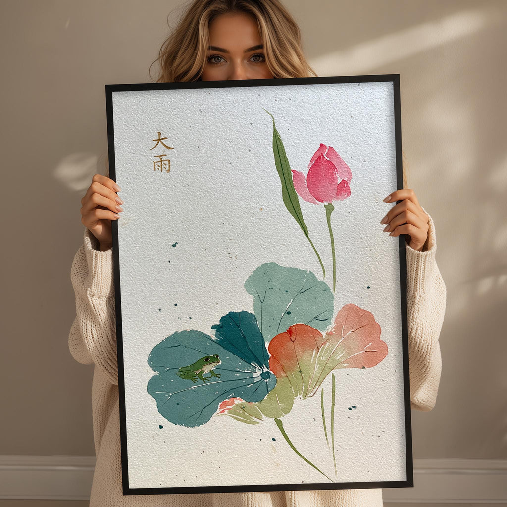 A woman is holding up a framed print with a floral design featuring a pink rose, green leaves, and a frog.