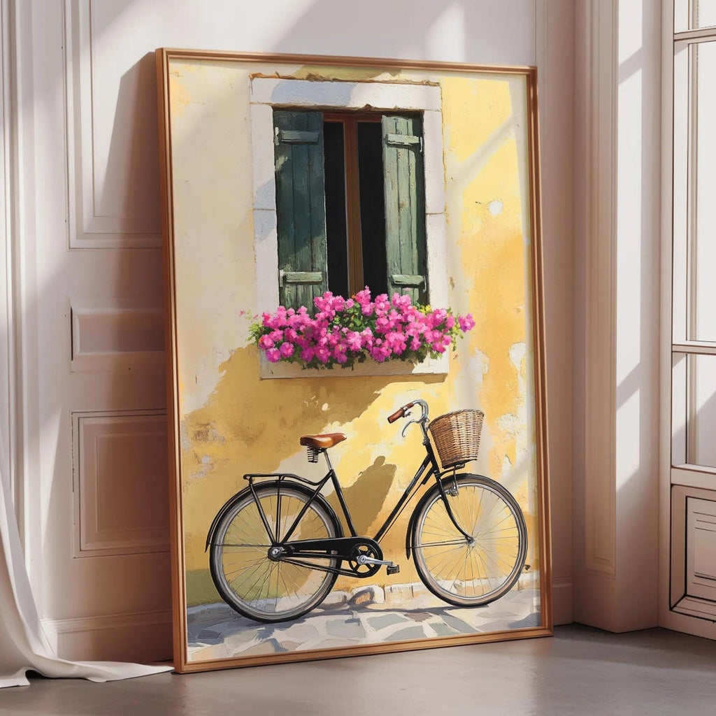 A framed painting depicting a bicycle parked in front of a yellow building with a window and pink flowers.