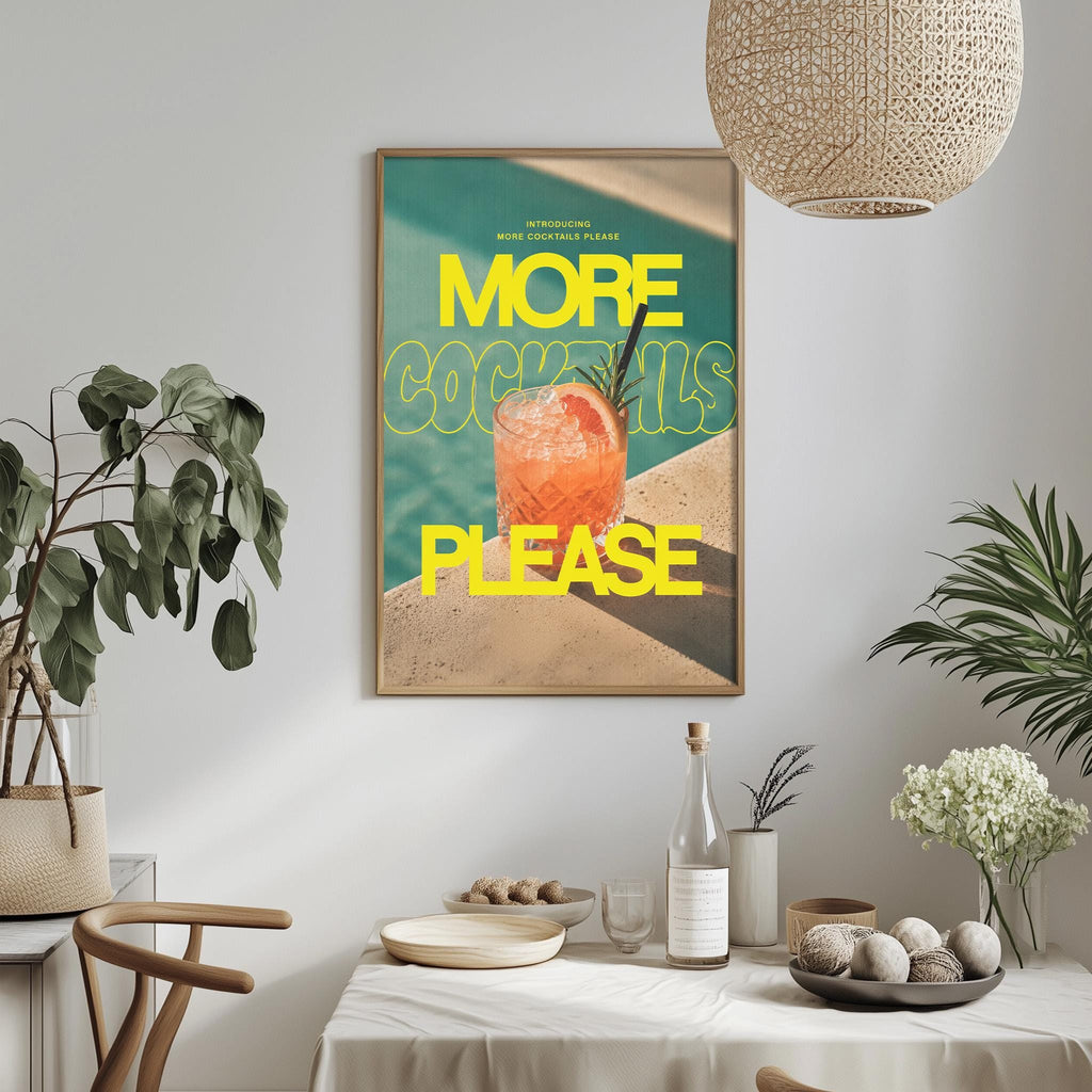 a framed poster with the text "MORE COCKTAILS PLEASE" hanging on a wall above a dining table with various items on it.
