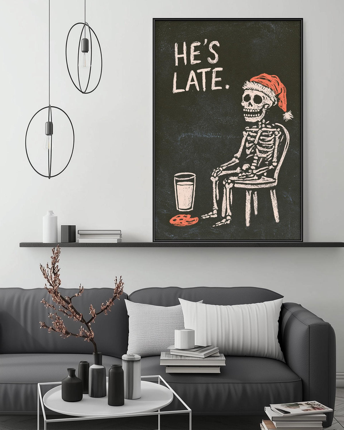 a black and white illustration of a skeleton wearing a Santa hat, sitting in a chair and holding a glass of milk. The skeleton is depicted in a playful and whimsical manner, adding a touch of humor to the scene. The image is displayed on a wall above a gray couch, creating a cozy and festive atmosphere in the living room.