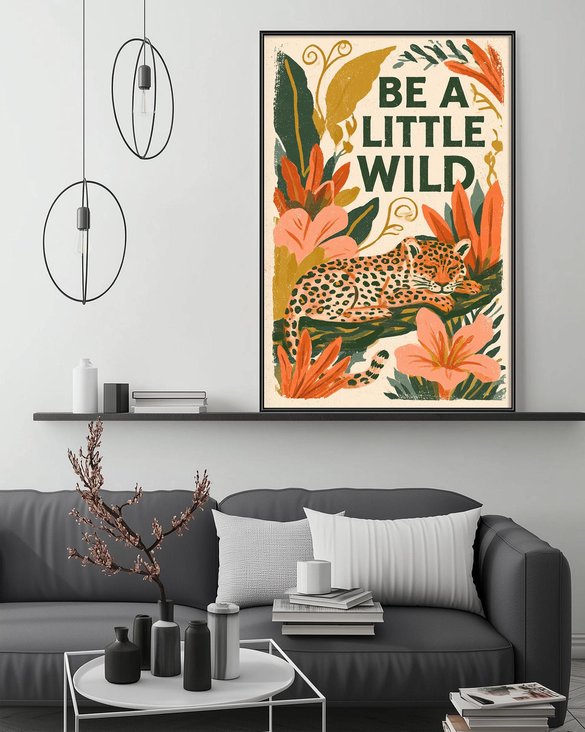 a living room with a gray couch, a coffee table, and a framed poster of a leopard resting on a leaf-filled background. The poster has the text "Be a little wild" written on it.