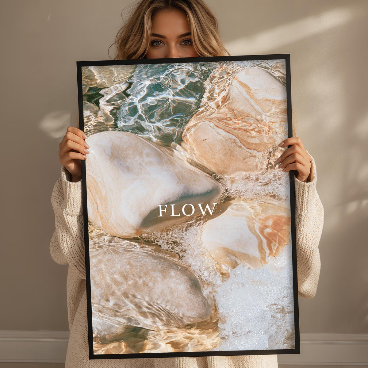 A woman holding a framed print with a water-themed image, including rocks and water.