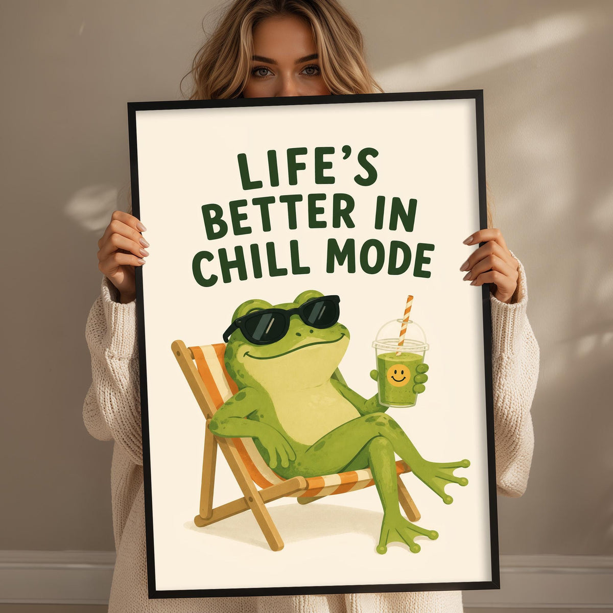 A woman is holding up a framed poster with a cartoon image of a frog sitting in a chair and holding a drink.
