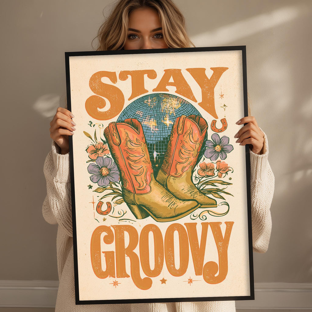 A woman holding a framed poster with the text "STAY GROOVY" and an illustration of a pair of cowboy boots.