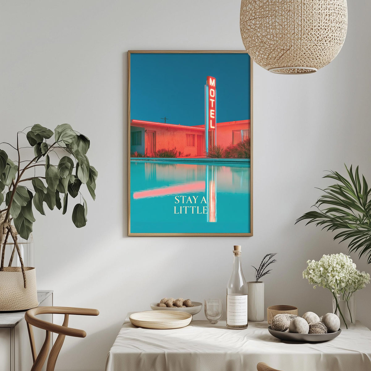 a framed poster of a motel with a neon sign, hanging on a wall above a dining table with various decorative items and plants.