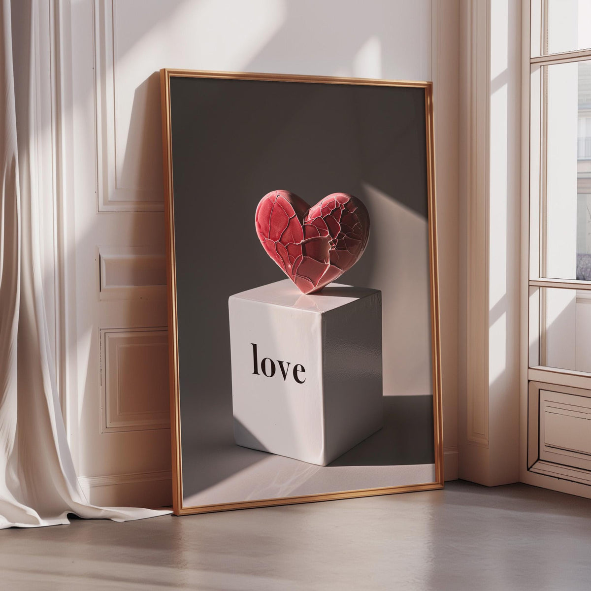 A framed image of a red heart-shaped object on a white block with the word "love" written on it, placed on a wooden floor in a room with a window.